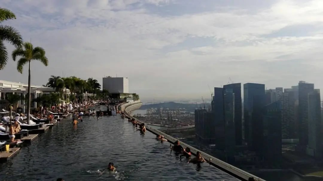 Ein Infinity Pool auf einer Dachterrasse in Singapur mit Blick auf die Skyline und den Hafen im Hintergrund.