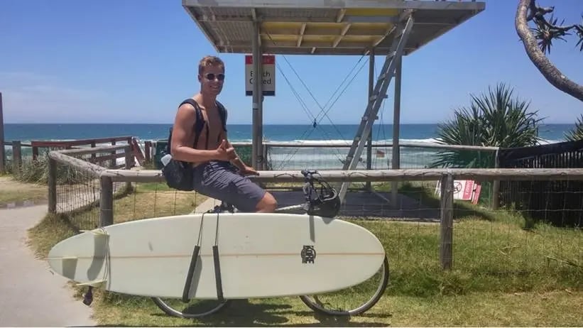 Student der Bond University mit Surfboard vor malerischer Strandkulisse.