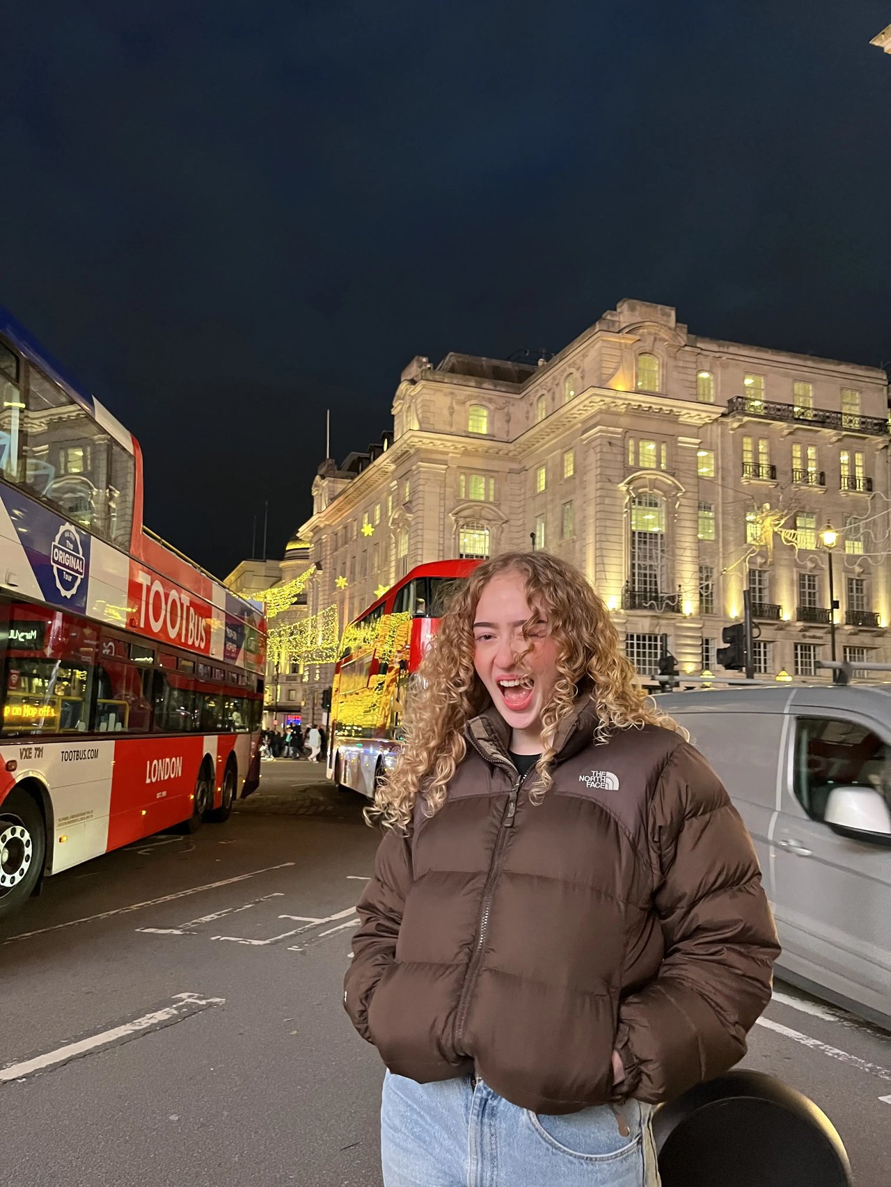 Londons belebte Straßen bei Nacht mit roten Doppeldeckerbussen und einer lächelnden Studentin, Großbritannien.