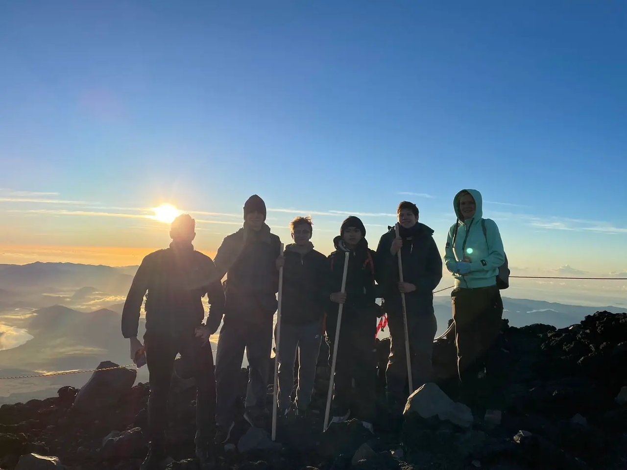 Gruppe von Studierenden bei Sonnenaufgang auf dem Gipfel des Mount Fuji, Japan.