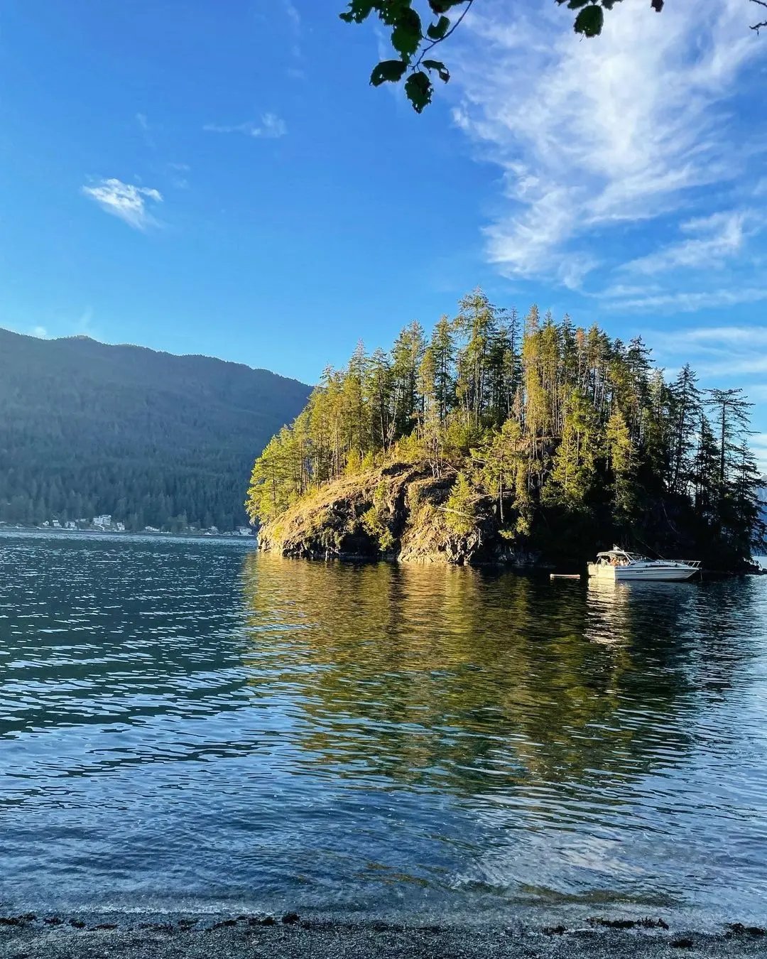 Malerische Insel mit Boot auf einem ruhigen See umgeben von Wäldern in British Columbia, Kanada.