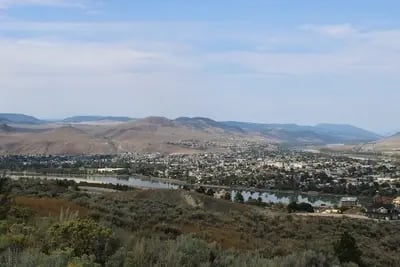 Panoramablick auf die Stadt Kamloops, Kanada, mit einem Fluss, Hügeln und klarer Sicht.