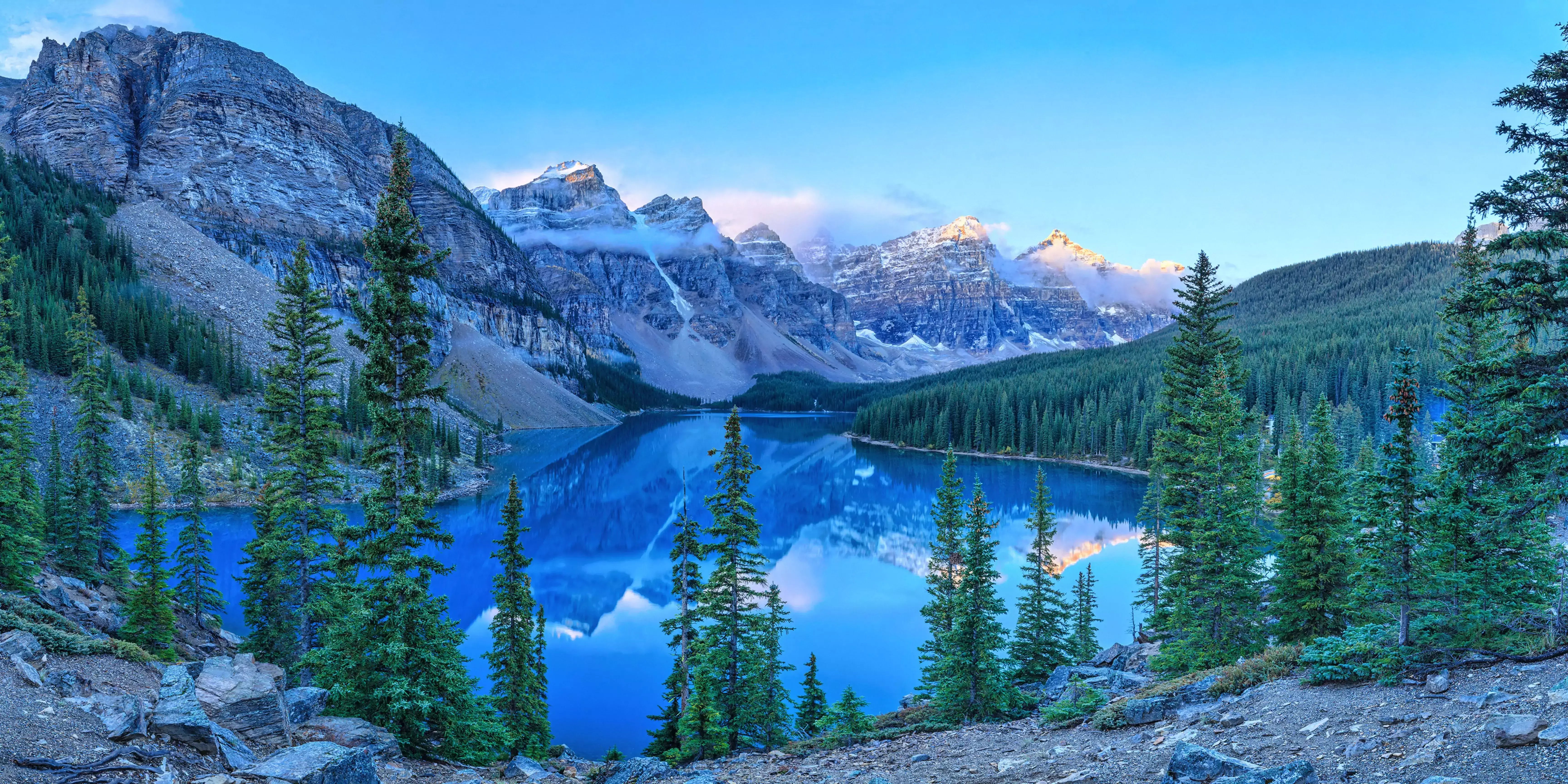 Atemberaubende Landschaft in Kanada mit klarem, spiegelndem See, umgeben von dichten Nadelwäldern und schneebedeckten Bergen im Hintergrund.
