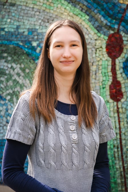 Maria Zasadzki vom IEC Online Team lächelt vor einer bunten Mosaikwand.