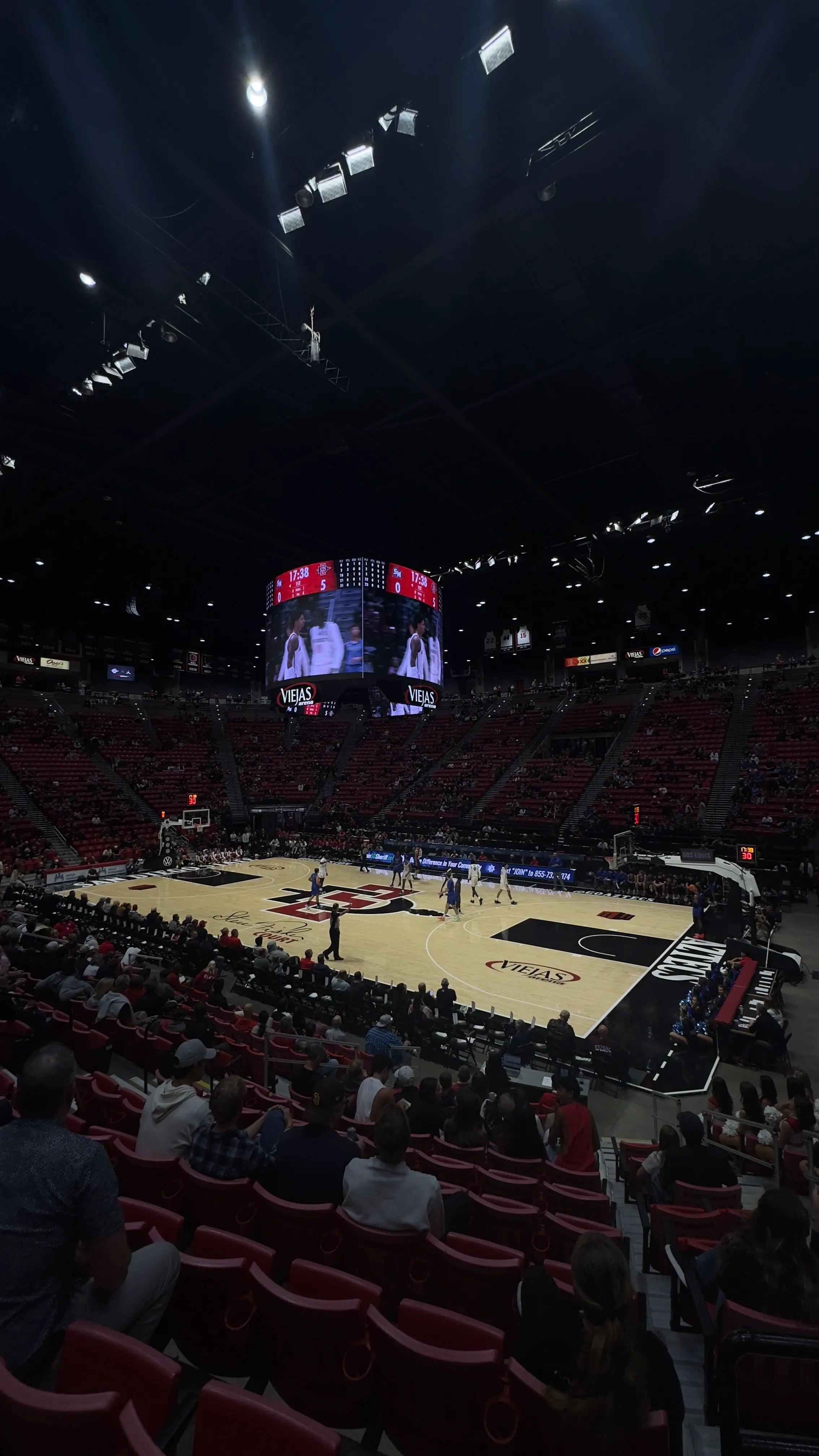 Basketballspiel in einer großen Arena mit Zuschauern und leuchtender Anzeigetafel.