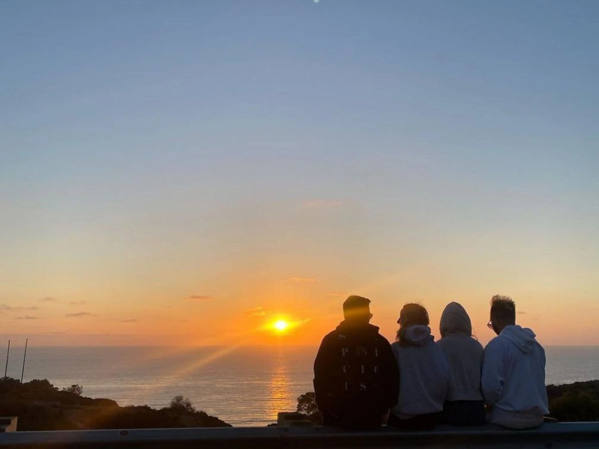 Freundesgruppe, die gemeinsam den Sonnenuntergang über dem Meer in San Diego genießt.