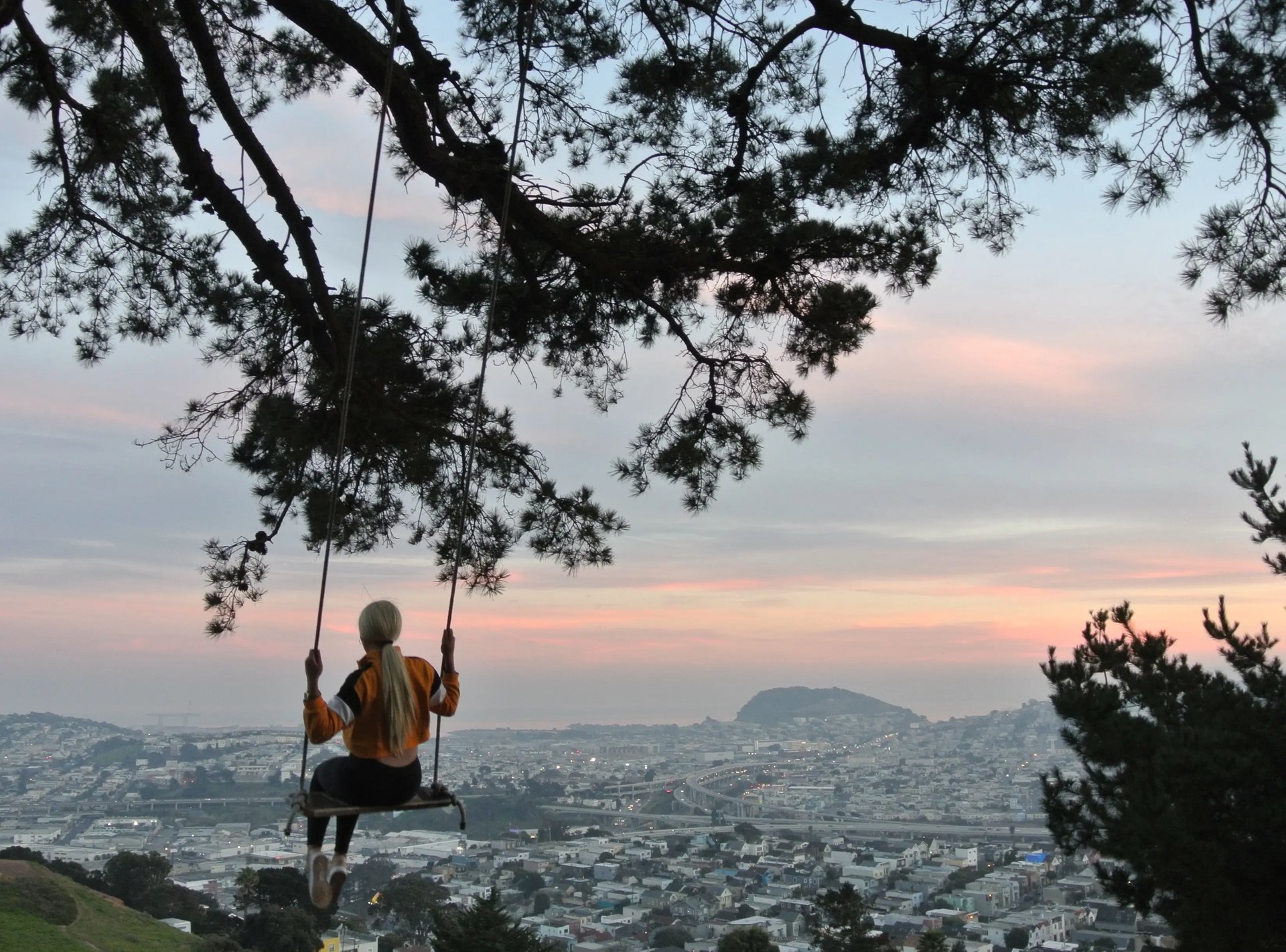 Studentin schaukelt im Bernal Heights an einem Baum mit Blick auf San Francisco bei Sonnenuntergang.